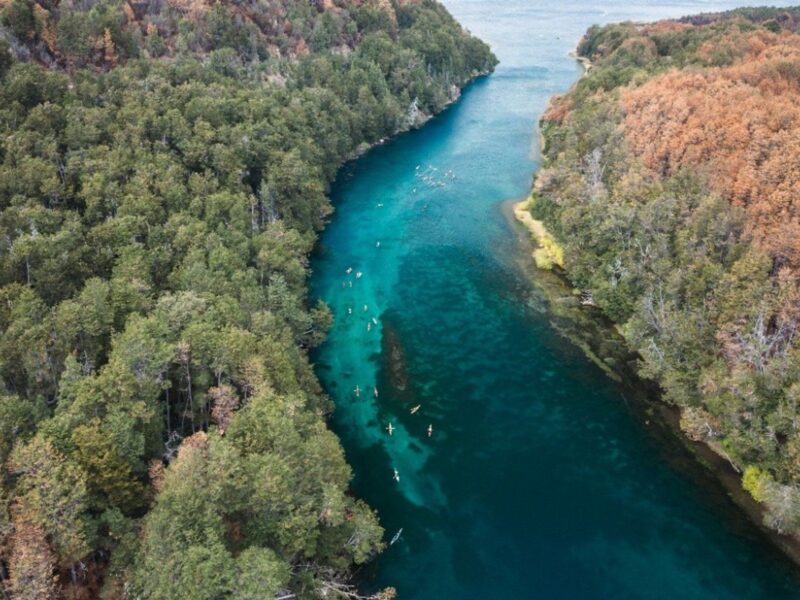 Vista aérea de kayakistas remando por el río Arrayanes, de aguas turquesa entre bosques, durante la Bajada de los Lagos en el Parque Nacional Los Alerces