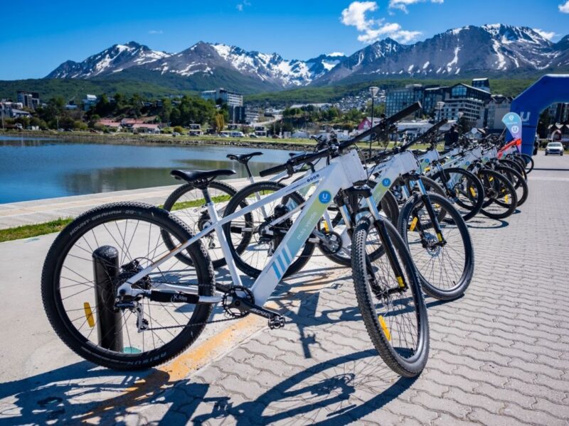 Bicicletas públicas de BiciUshuaia estacionadas en la costanera de Ushuaia con la bahía y los montes Martial de fondo