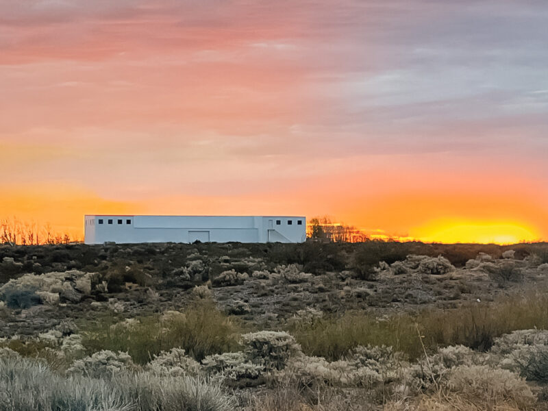 Edificio blanco de la Bodega Patritti al atardecer, entre la vegetación de la estepa en San Patricio del Chañar, Neuquén