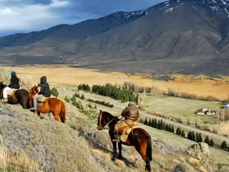Jinetes a caballo en un mirador sobre el valle, con cerros nevados de fondo, cerca de Esquel, Chubut