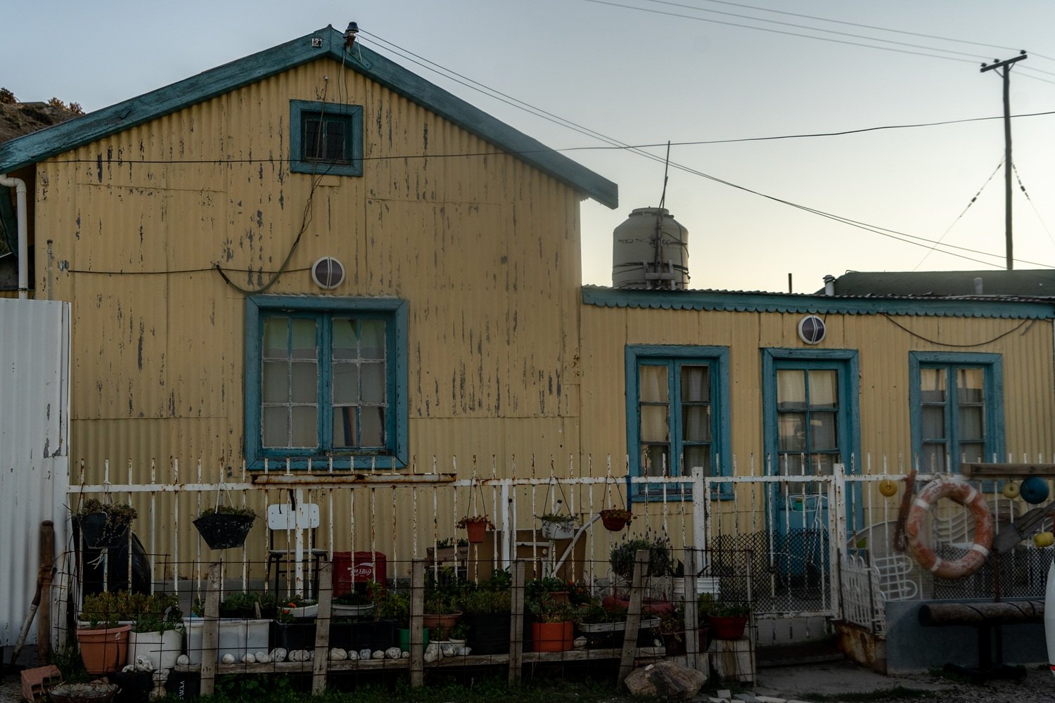 Casa de chapa amarilla con ventanas turquesa y plantas en Caleta Córdova, pueblo de pescadores de Comodoro Rivadavia