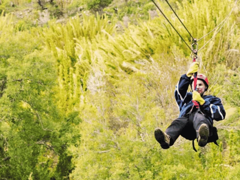 Persona deslizándose por un cable de canopy sobre el bosque verde de Pueblo Alto Lodge, cerca de Esquel y del Parque Nacional Los Alerces