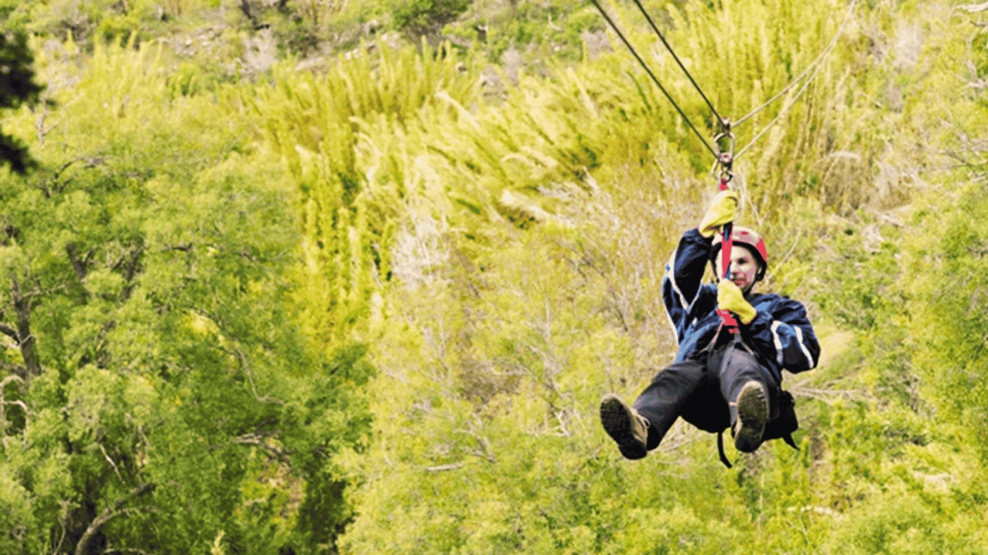 Persona deslizándose por un cable de canopy sobre el bosque verde de Pueblo Alto Lodge, cerca de Esquel y del Parque Nacional Los Alerces