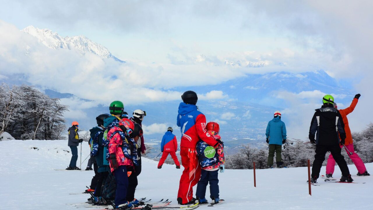 Grupo de esquiadores en la pista del Cerro Perito Moreno con vista al valle de El Bolsón y la cordillera nevada