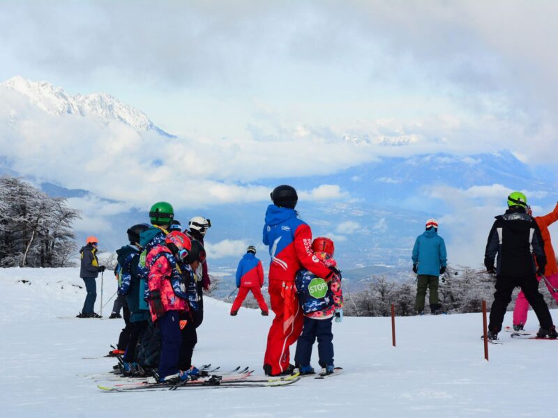 Grupo de esquiadores en la pista del Cerro Perito Moreno con vista al valle de El Bolsón y la cordillera nevada