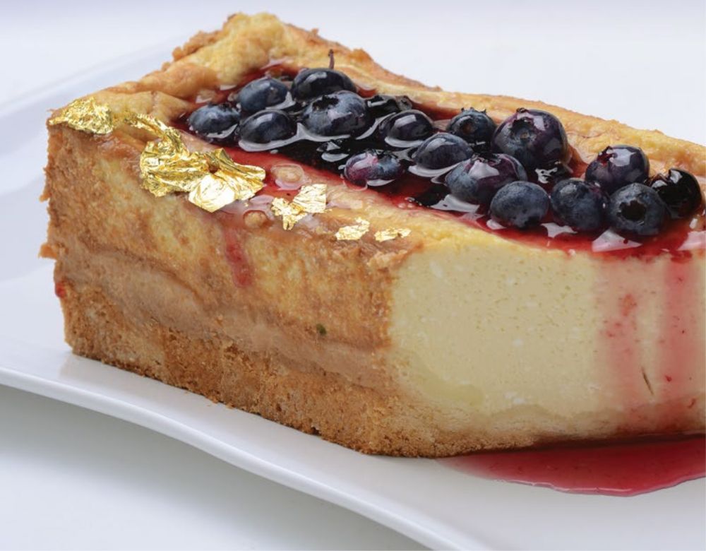 Porción entera de cheesecake tibio con base de galletitas y miel, cubierta con salsa de calafate