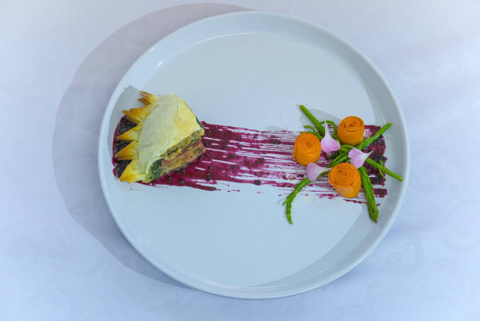 Plato de autor con hojaldre, espárragos, rollos de zanahoria y salsa de frutos rojos