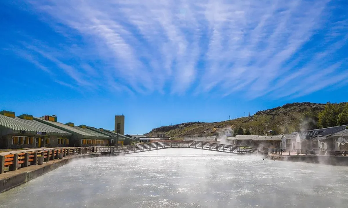 Pileta termal humeante y edificios del Complejo Termal Copahue bajo cielo azul, en el norte neuquino