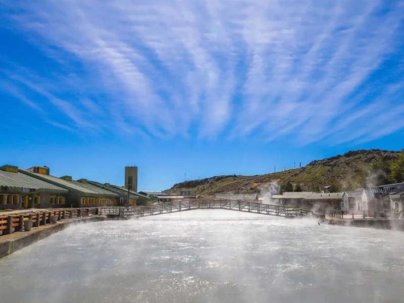 Pileta termal humeante y edificios del Complejo Termal Copahue bajo cielo azul, en el norte neuquino