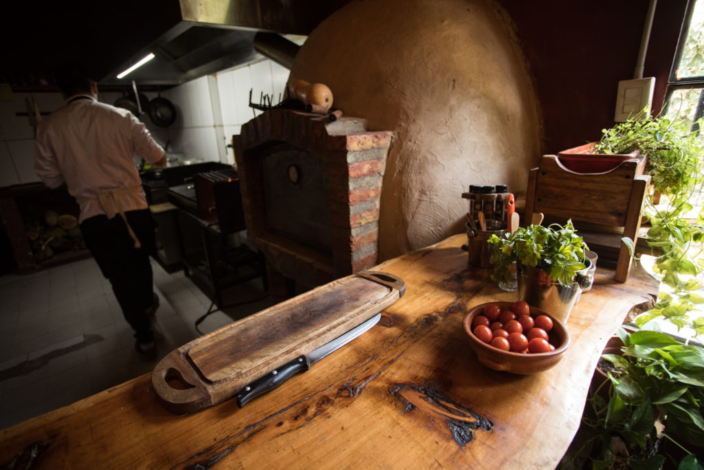 Cocina de El Viejo Molino de Dolavon con horno de barro, mesada de madera y tomates frescos