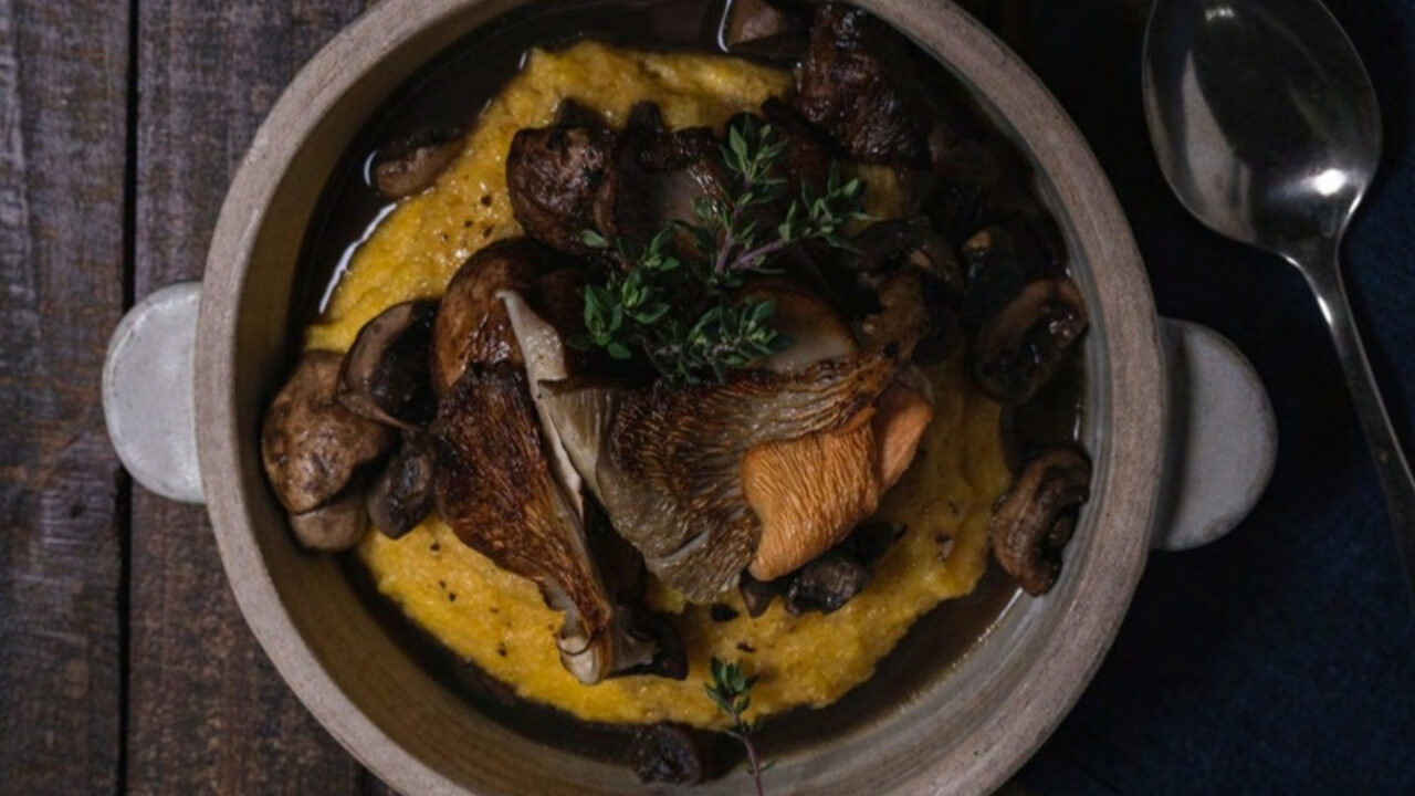 Estofado de gírgolas, shiitakes y champiñones sobre polenta cremosa en una cazuela de cerámica