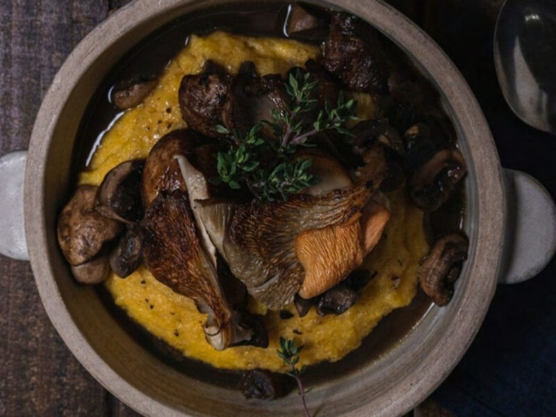 Estofado de gírgolas, shiitakes y champiñones sobre polenta cremosa en una cazuela de cerámica