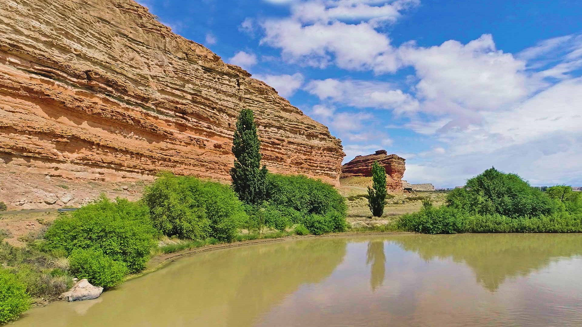 Farallón de areniscas rojizas junto a un remanso del río Chubut, con álamos, en el Área Natural Protegida Los Altares