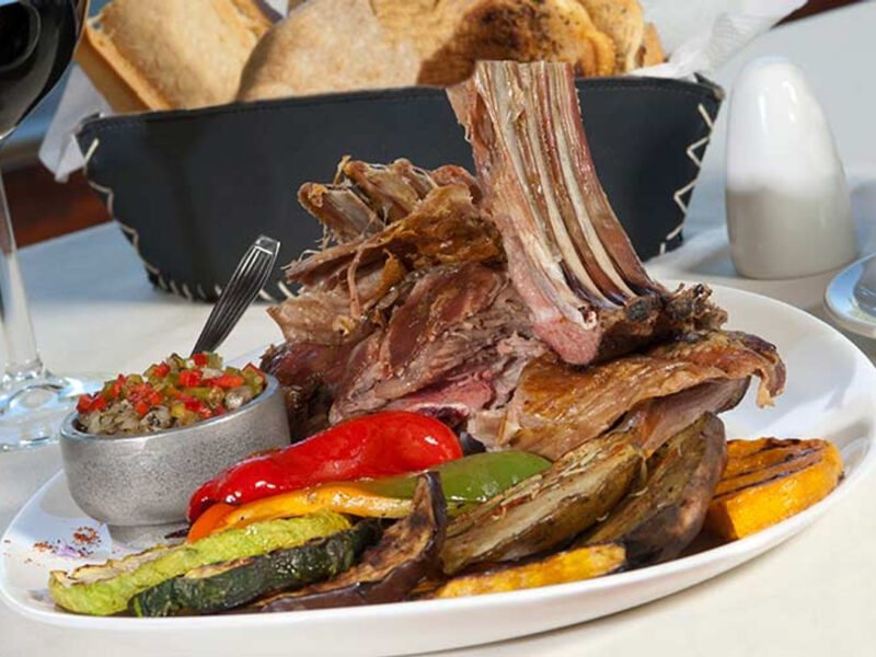 Cordero patagónico a la parrilla con verduras asadas y copa de vino tinto en La Tablita, El Calafate