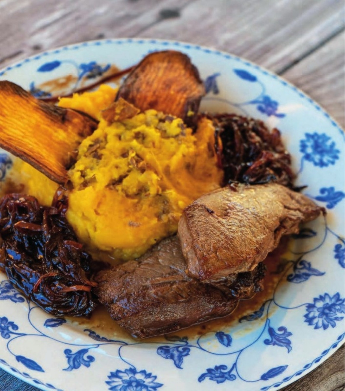 Plato con lomo de guanaco, puré de batata y cebolla caramelizada sobre vajilla azul y blanca