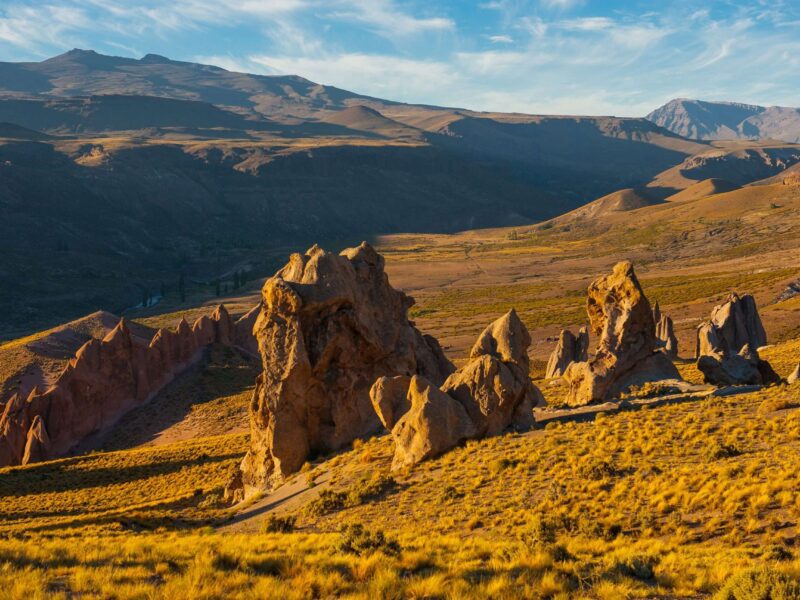 Formaciones rocosas de Los Bolillos sobre la estepa dorada de Varvarco, con la cordillera del norte neuquino de fondo