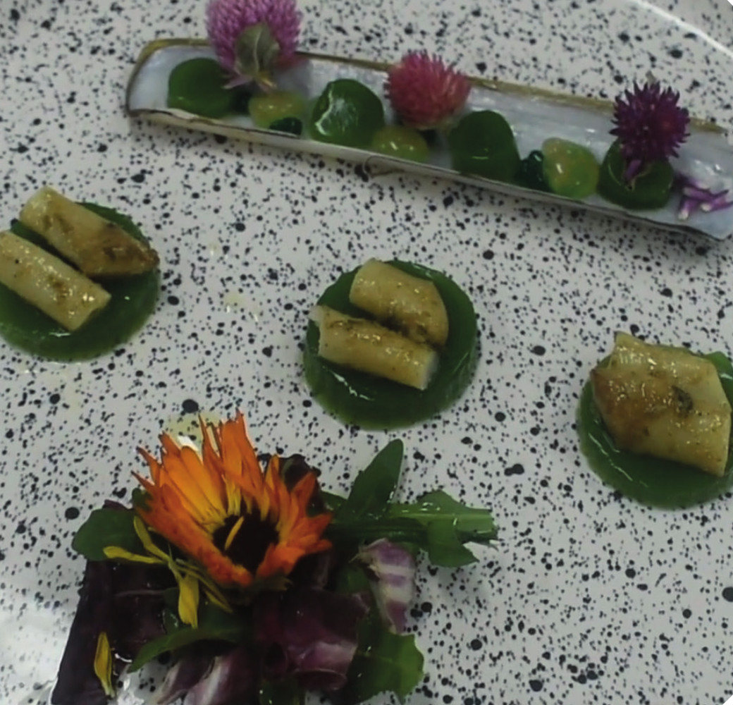 Emplatado de navajas de mar con velo de rúcula, flores comestibles y la valva como bandeja