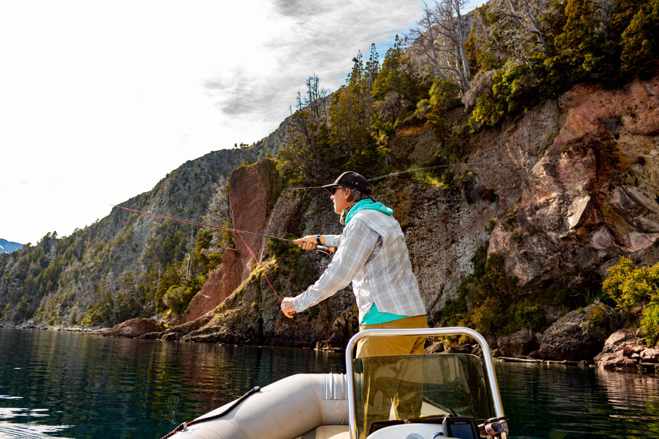 Pescador lanzando con caña de mosca desde un bote frente a los acantilados del lago Nahuel Huapi, en Villa La Angostura