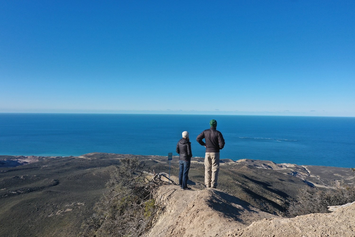 Dos caminantes contemplan el mar desde un mirador del Área Natural Protegida Rocas Coloradas, Comodoro Rivadavia