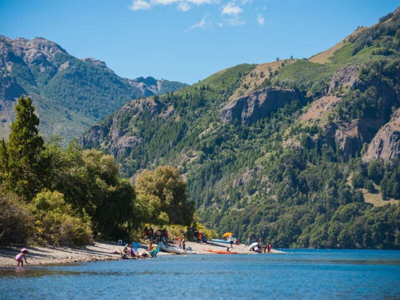Familias en la playa de Quila Quina, a orillas del lago Lácar, con cerros boscosos del Parque Nacional Lanín, Neuquén