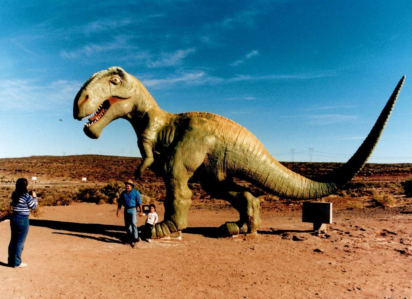 Familia sacándose fotos junto a la réplica de dinosaurio en la estepa de Villa El Chocón, Neuquén